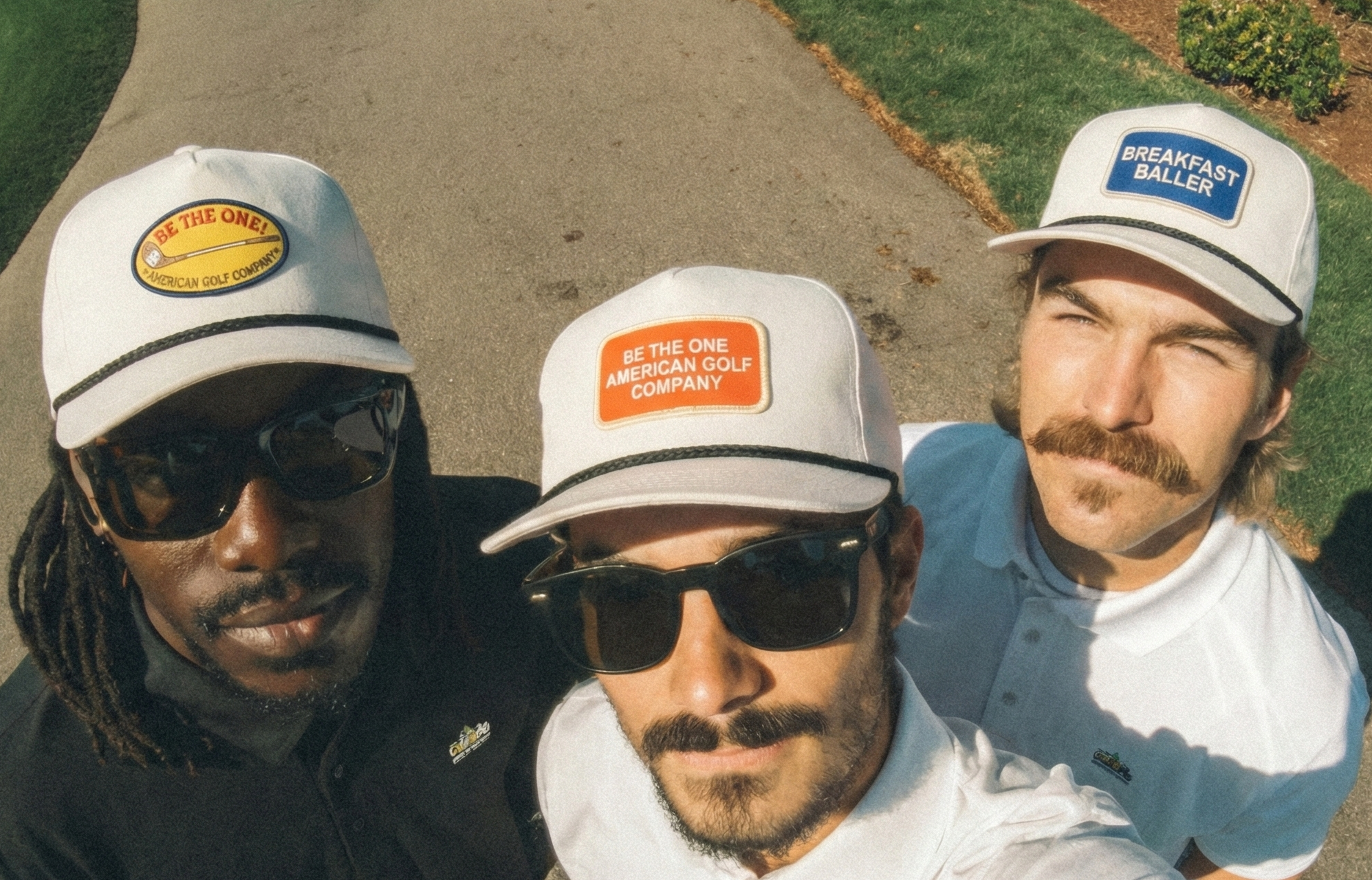 Three men wearing branded caps taking a selfie outdoors.